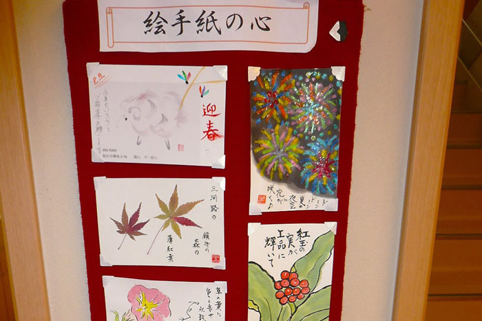 入居者の手作り絵画作品を展示した壁面。季節の花や風情ある作品が掲示されている。